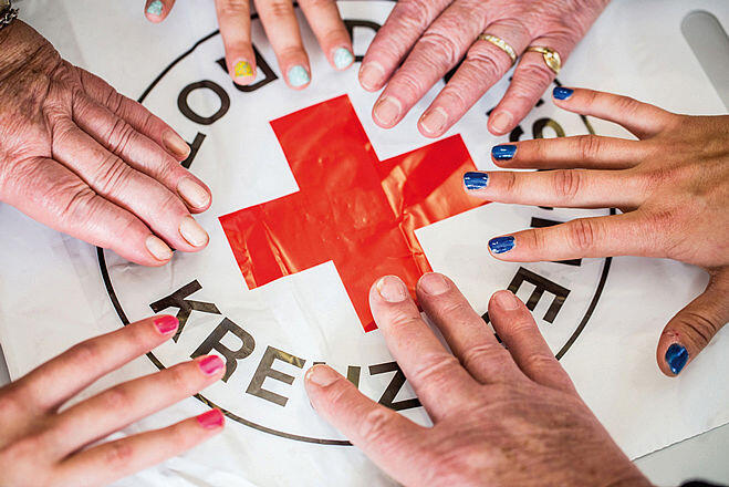 Bild: viele Hände berühren das Rote Kreuz Symbol
